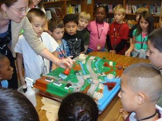 Children standing around a table watching a teacher demonstrate how stormwater works